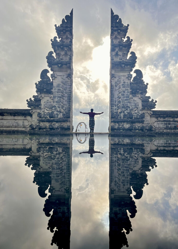 Man stands between two temple structures with his image reflected in water