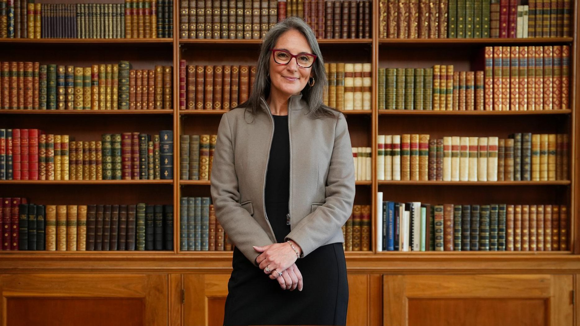 Portrait of a white woman in a suit standing in front of a large bookcase.