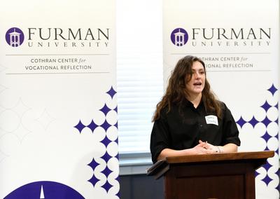 white woman with dark hair wears black shirt and stands at podium.