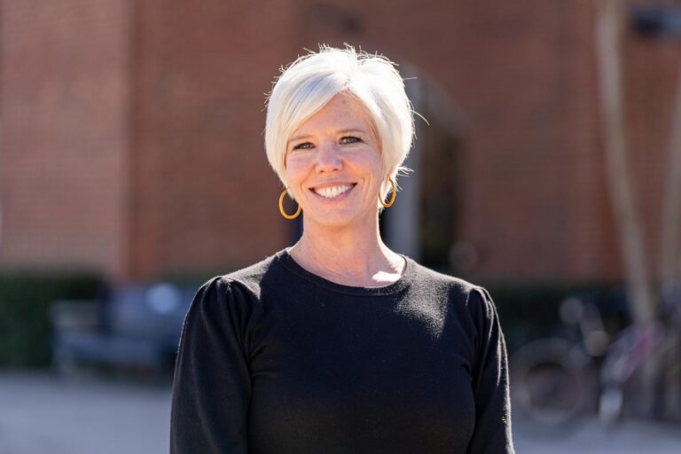 A white woman with short white hair, wearing a black top, stands outside.