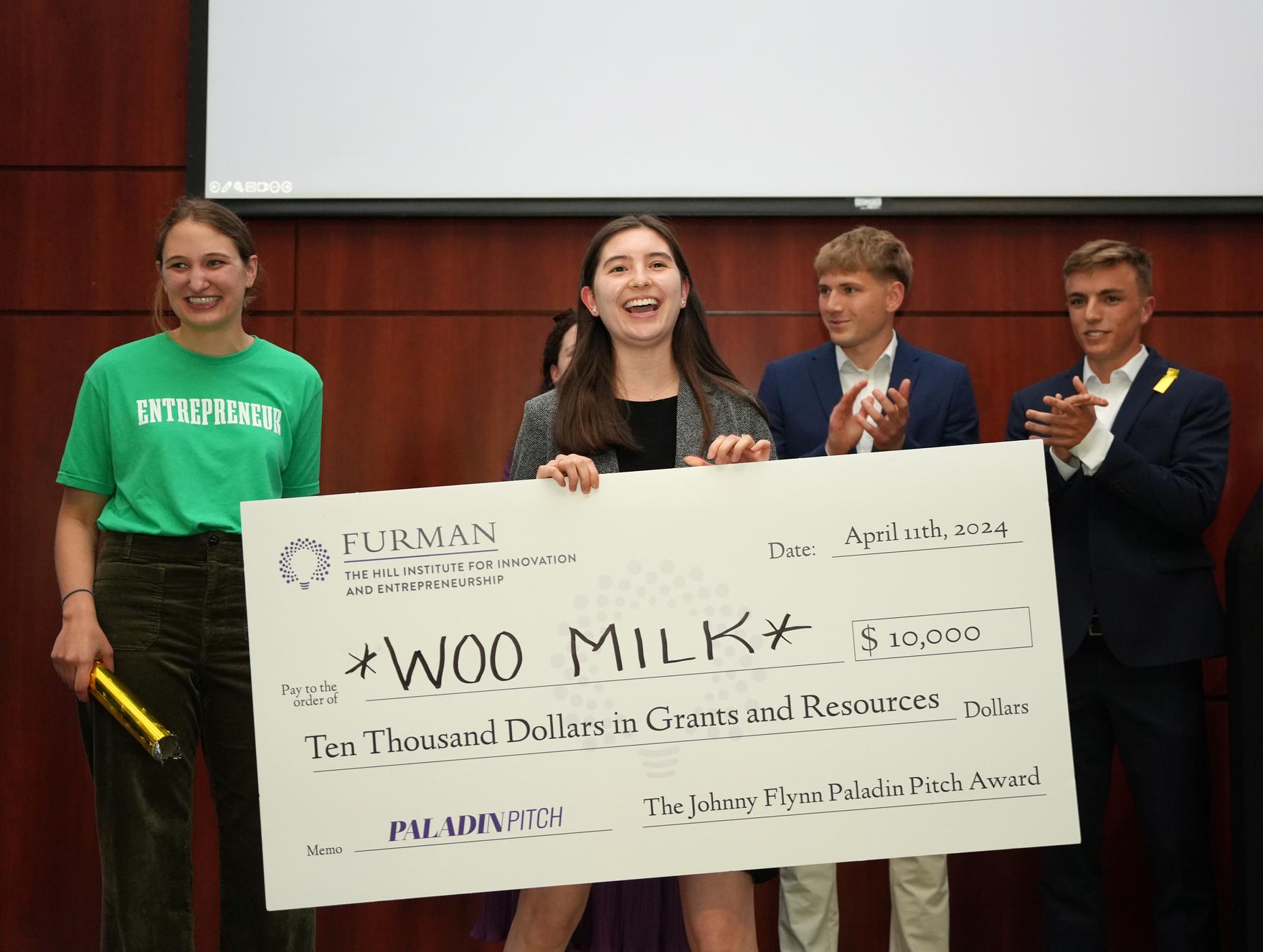 A young woman holds a large check for $10,000 while people look on.