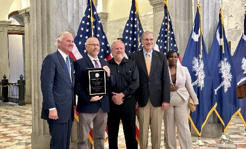 four white men and one black woman stand in front of U.S. flags in SC Statehouse