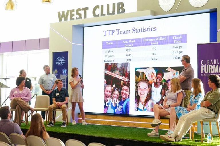 Several people stand around a large display board during a presentation.