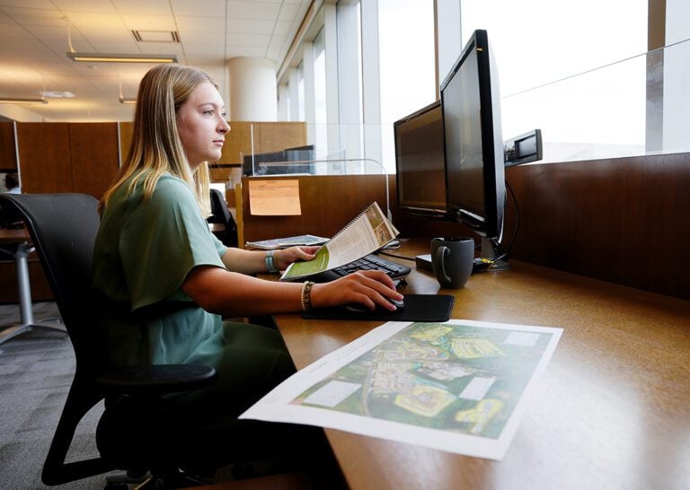 A young white lady with blonde hair works at a computer.