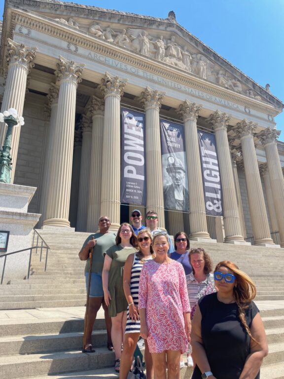 Nine adults stand on the steps outside the National Archives.