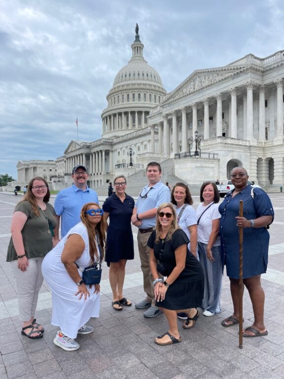 Nine adults stand outside the Capitol in Washington D.C. The Capitol Dome is in the background.