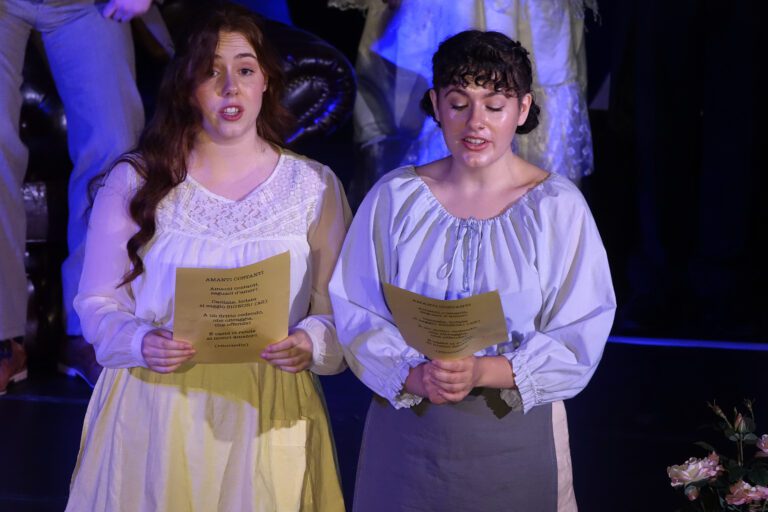 Two young women in costume sing opera on a stage.