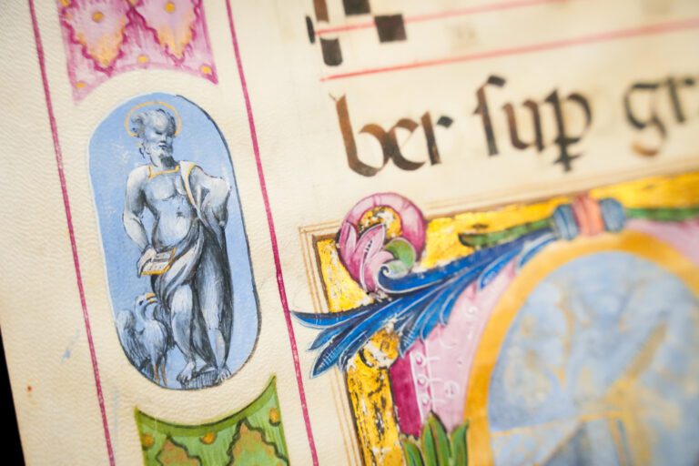 Close up photo of a manuscript with artwork in the corner and bright yellow, blue, pink and green colors.