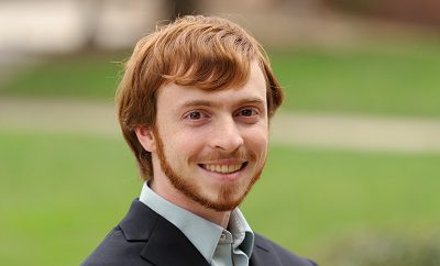 white man with red hair and beard wears suit outdoors