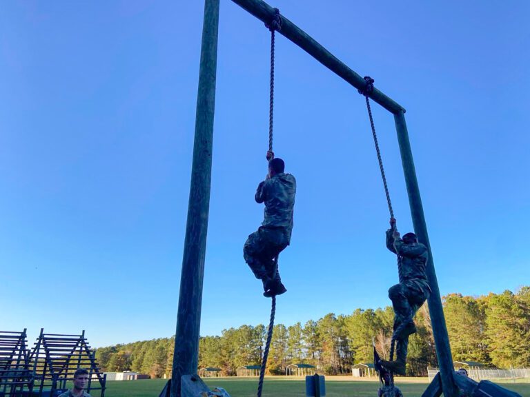 Cadets climb ropes on an obstacle course in early morning light. 