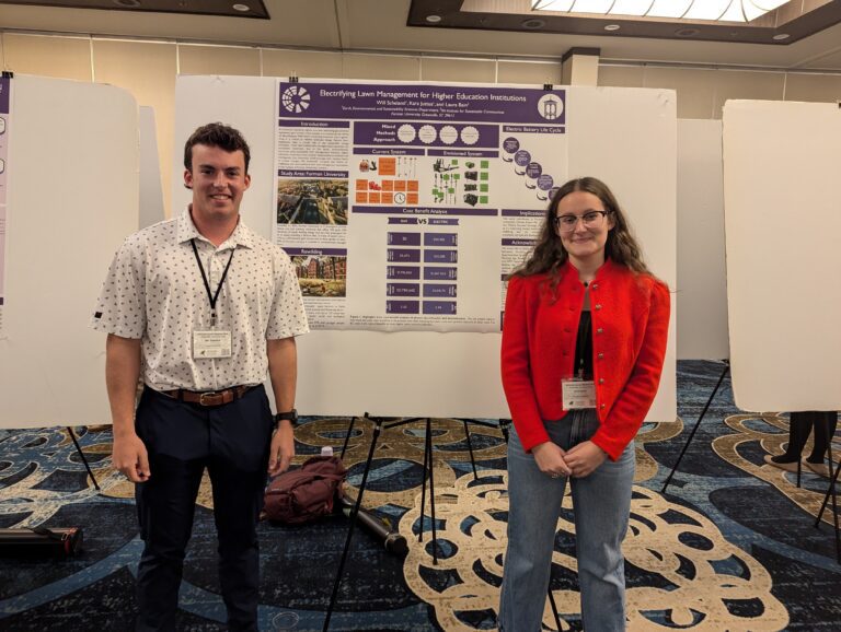 Two students stand in front of a poster displaying scientific research