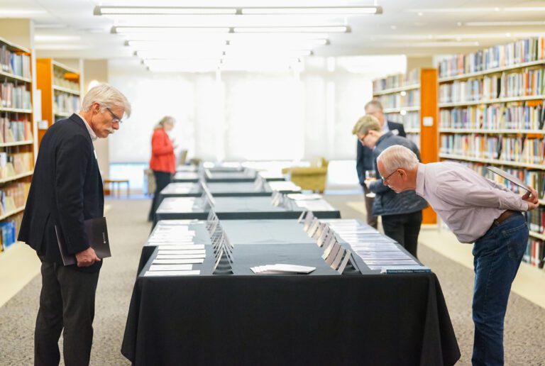 People stand on either side of a row of tables, leaning down to look at information printed on sheets atop each table.