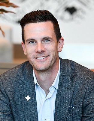 white man with dark hair wears sport coat in indoor photo