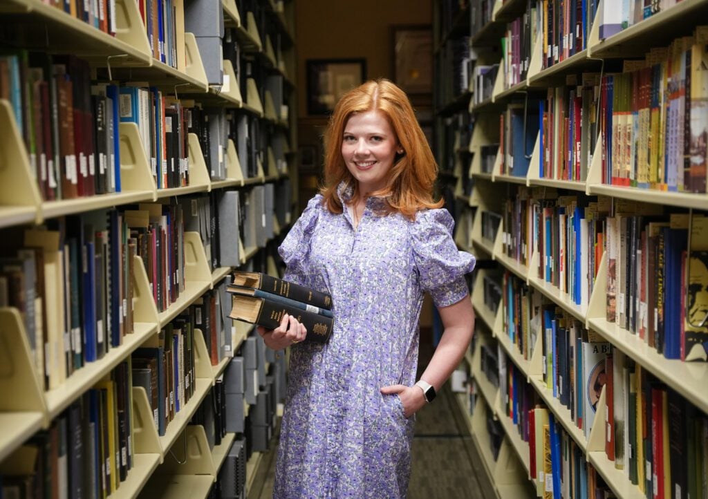 A female student stands among books in a library.