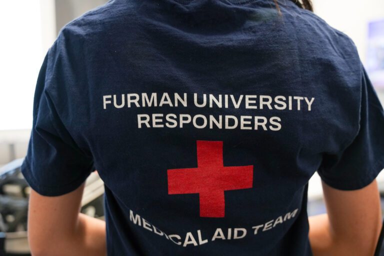 The back of a young woman's navy blue t-shirt, with a red cross printed on it and the words "Furman University Responders"