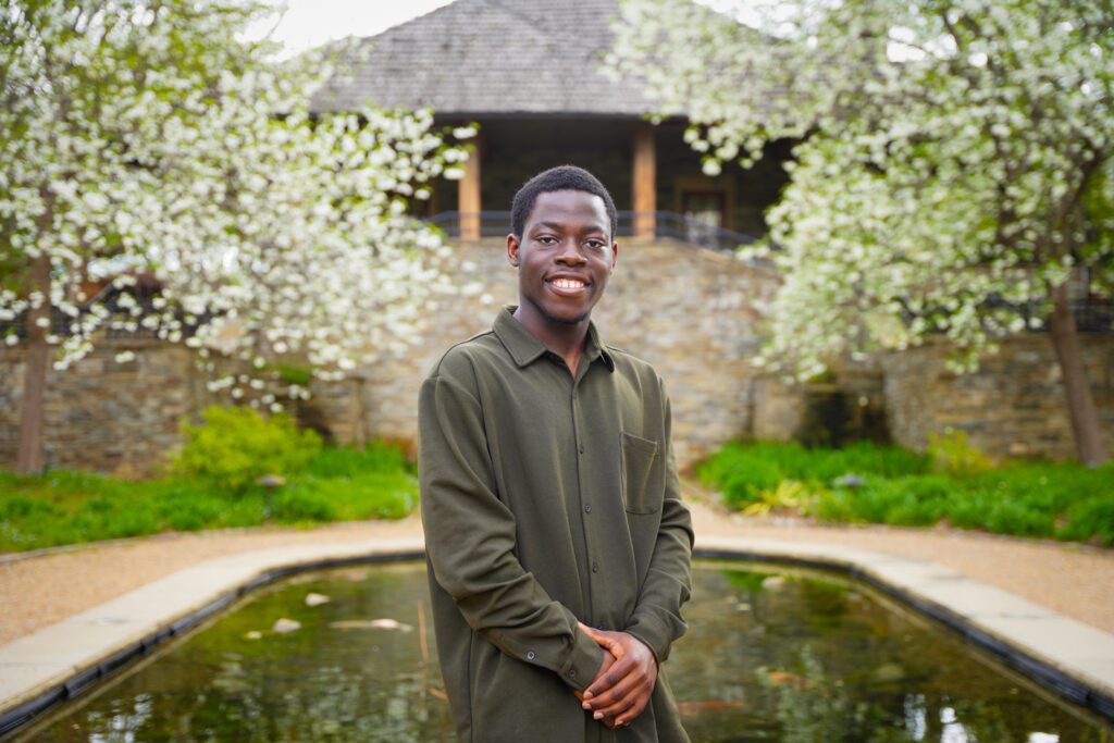 A male student stands outside surrounded by blossoming trees.
