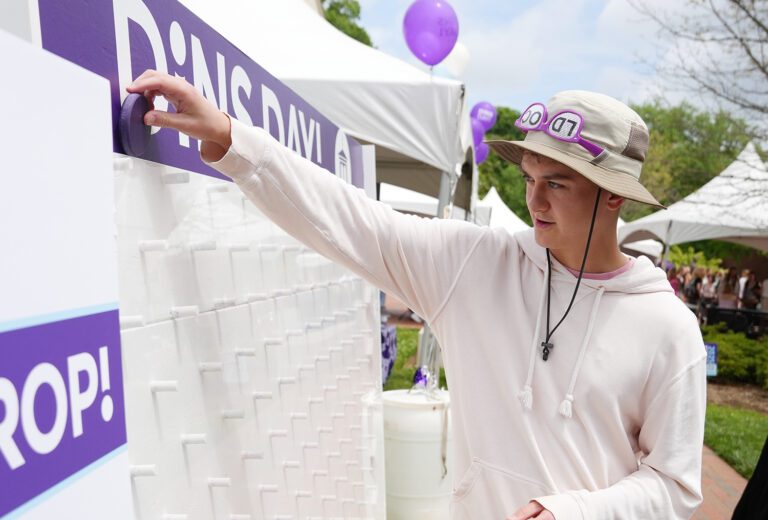 A young white man plays a game of "Plinko," dropping a token into a vertical peg grid