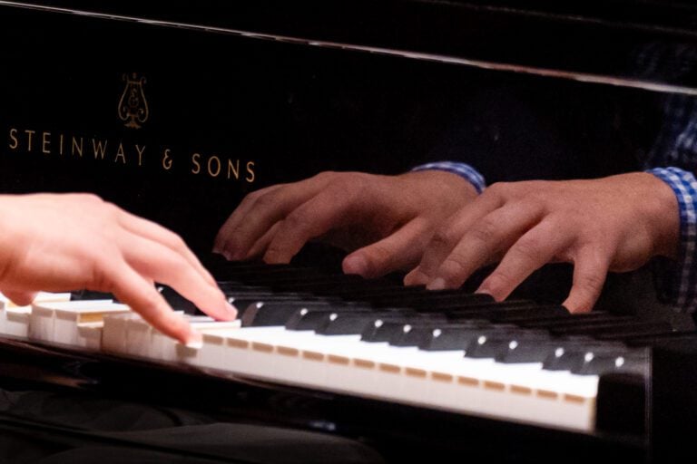 Hands playing the piano with a reflection of those hands appears in the piano. Etching shows it to be a Stienway and Sons piano.