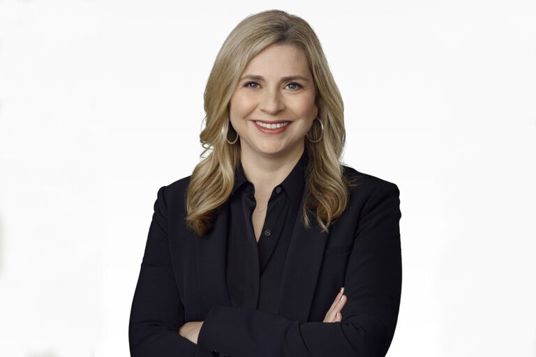 portrait of a white blonde woman in a dark suit and hoop earrings.