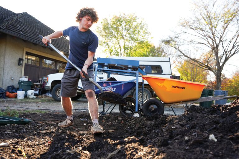 A young man sifts compost for debris into a yellow wheel barrow.