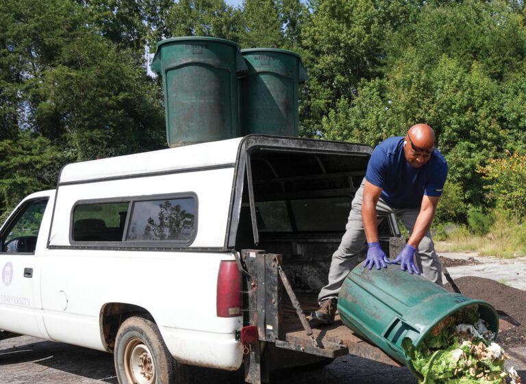 A man unloads organic waste from the back of a covered white pickup truck for compost.