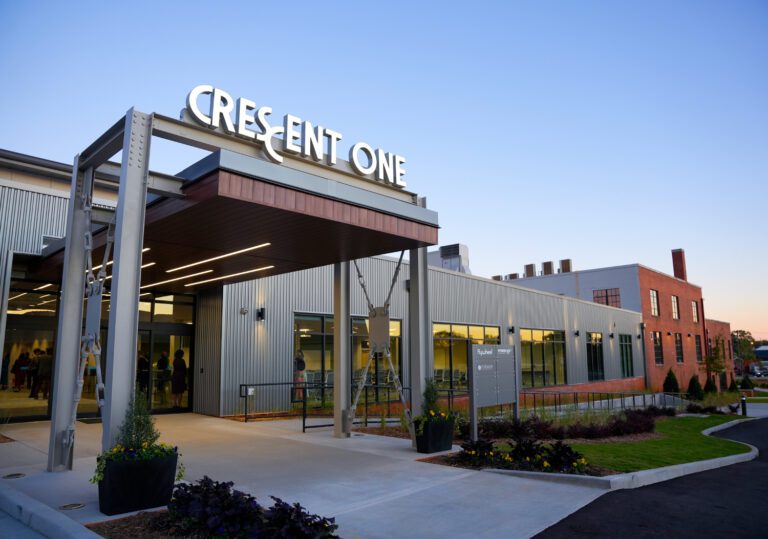 Entrance to a large building with green landscape and potted shrubs at sunset.