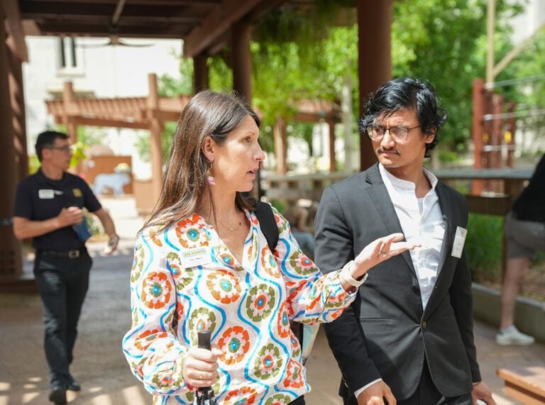 A young man in a suit speaks with a woman as they walk outdoors at a zoo.