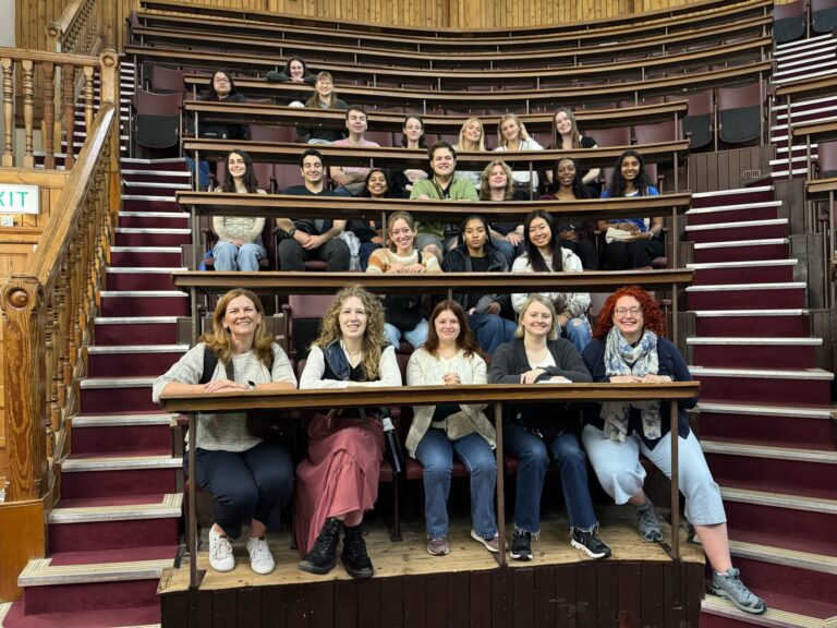 A group of students and faculty pose in the seats of a 19th Century surgical theater with old wooden stairs.