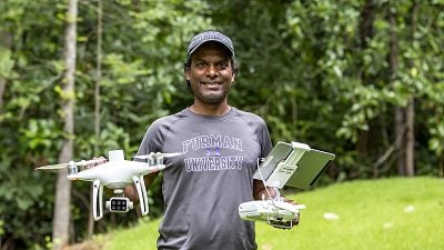 A man of color holds a drone in an outdoor photo.