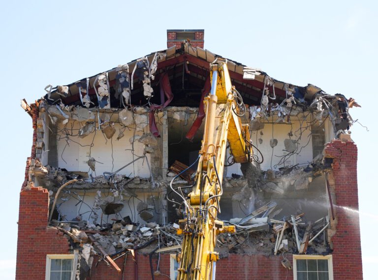 The exposed interior of a college dorm building, with its outer wall torn off by a yellow excavator demolishing Blackwell Hall on Furman University's campus.