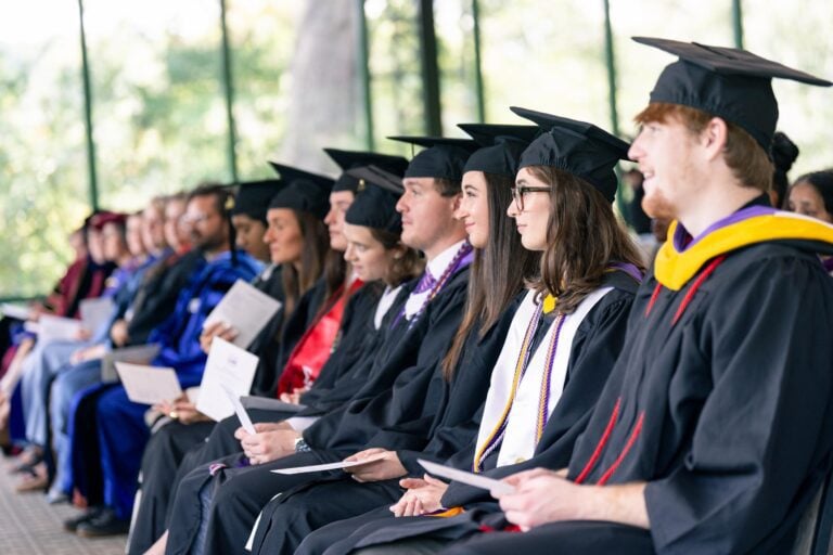 A row of students sit in graduation caps and gowns at Furman University's summer commencement ceremony.