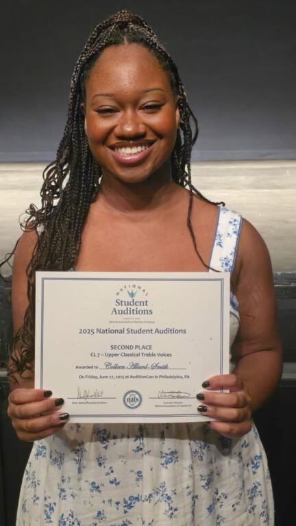 A young Black woman poses for the camera and holds up a certificate for winning second place.