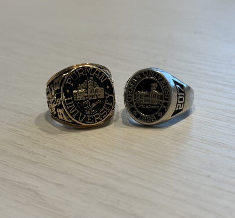 Two Furman University class rings sit on a table.