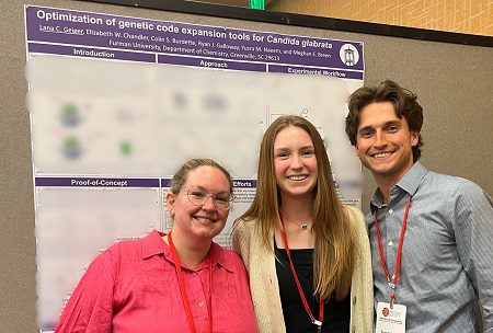 Three white people stand in front of a poster at The Protein Society Symposium.