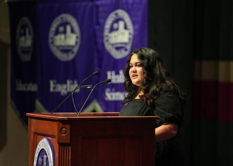 A young woman stands behind a lectern giving a speech at an indoor Convocation ceremony at Furman University.