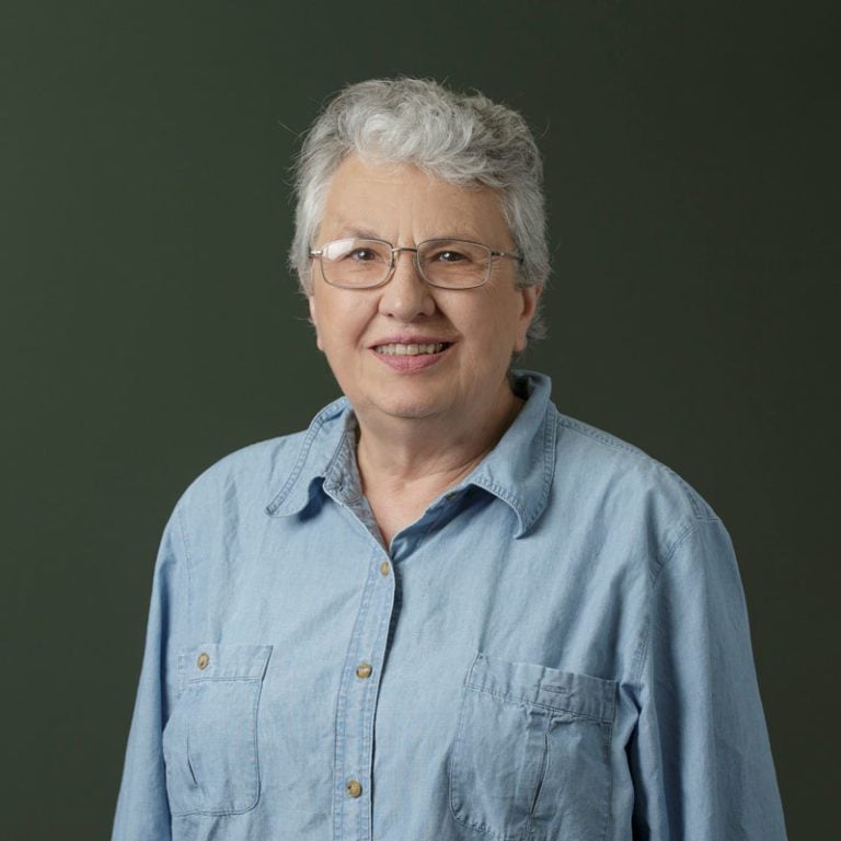A woman wearing glasses smiles on a blank background.