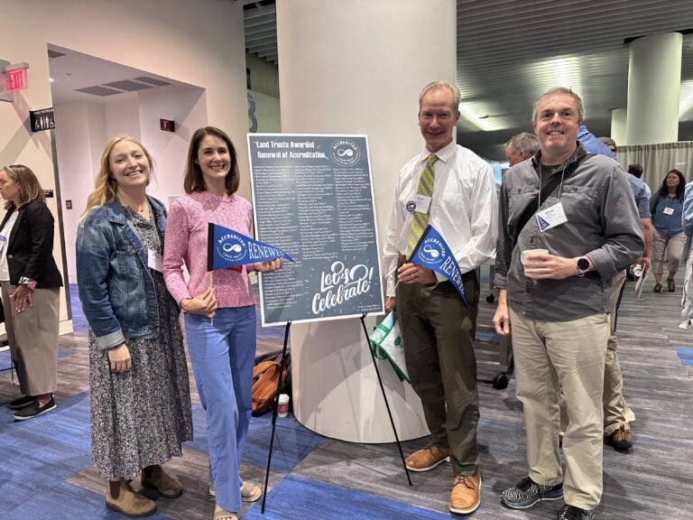 Two women and two men stand on either side of a poster, posing for a photo at an indoor conference event.