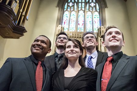 A Black man, three white men and a white woman dressed in formal attire stand in front of a stained-glass sanctuary window. SongFest