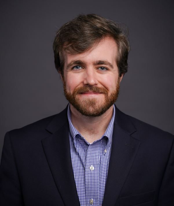 A profile image of a white man with a beard wearing a navy blazer.