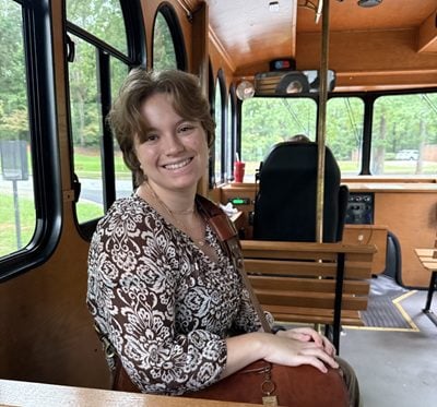 A white woman with short brown hair wears a patterned shirt and sits on a trolley. Campbell Romero '27