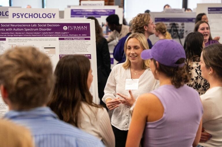 A crowd of people view dozens of poster presentations in a college campus building. Furman Engaged.