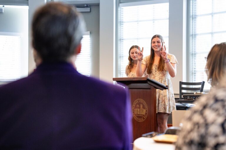 Two young women standing behind a lectern speak to a crowd at an award reception.