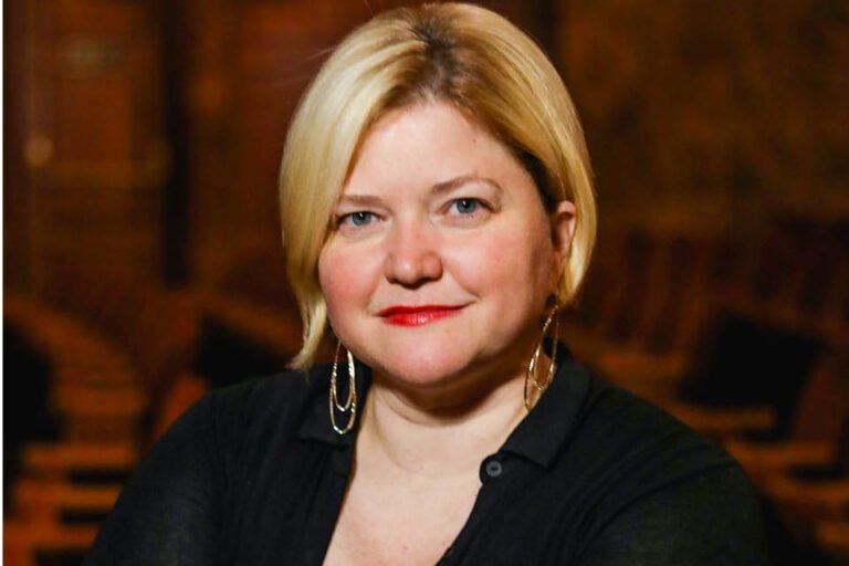 A portrait of a white woman wearing a black shirt with gold earrings and an ear-length haircut.