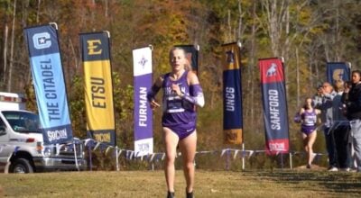 A woman runner with blond hair wears purple in an outdoor event.