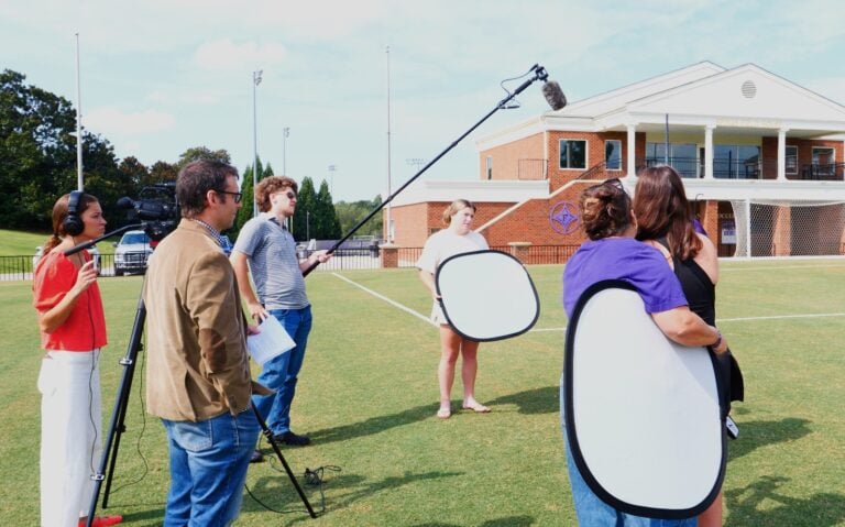 A group of young people film an interview in a soccer field.