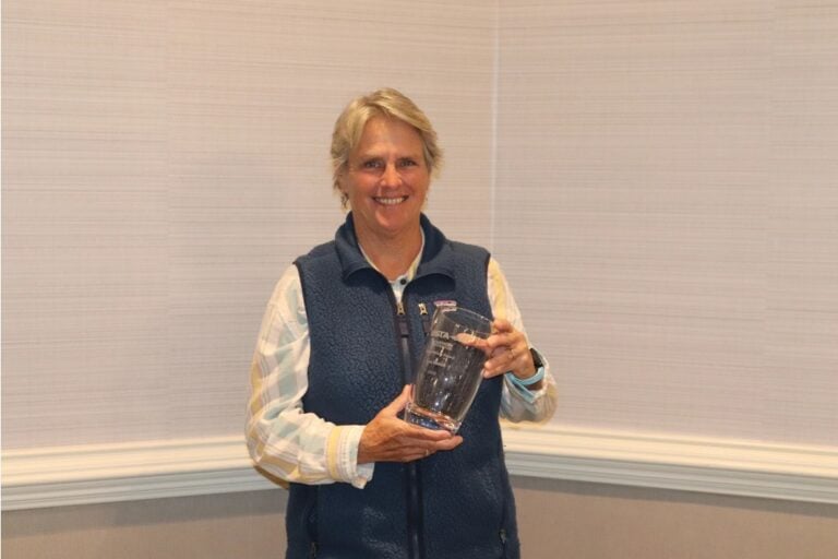 A portrait of a white woman in a blue vest holding a trophy