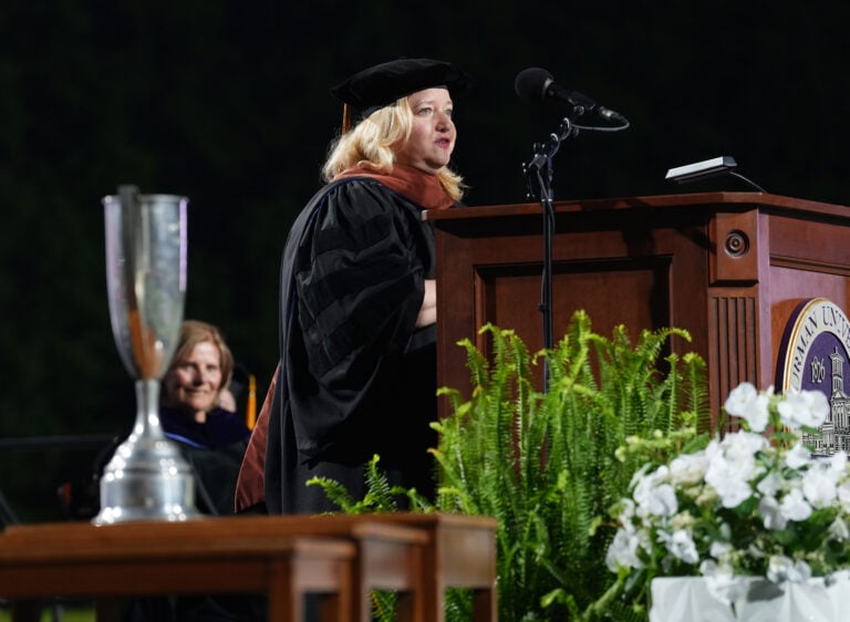 A woman gives a speech from behind a lectern, with a silver cup in the foreground.