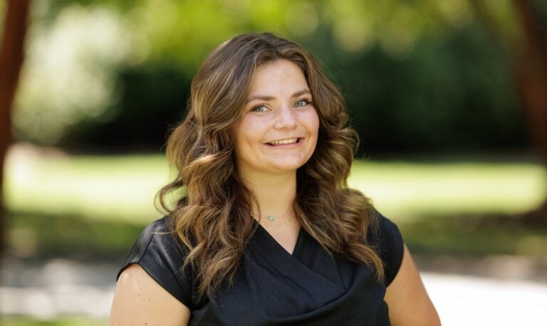 A white woman with long brown hair wears a black shirt in an outdoor photo. Libby Adams