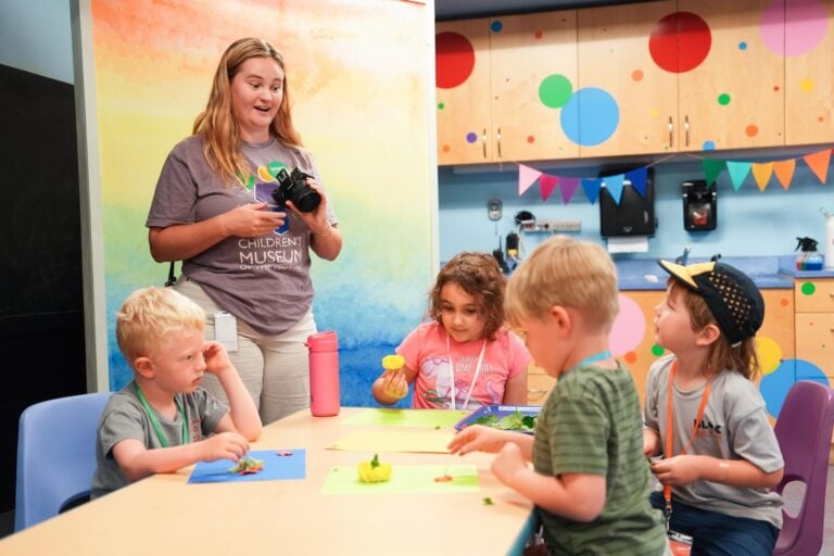 A young woman speaks with a group of children as they work on an arts and crafts project.