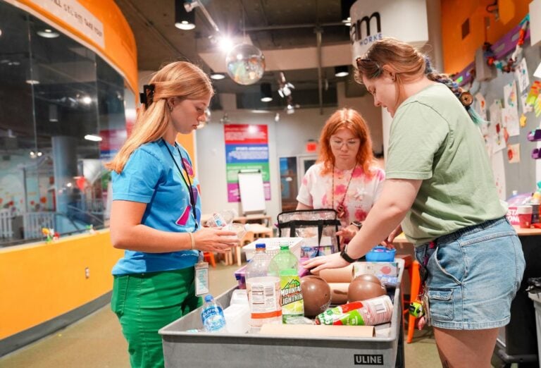 Two young women and their mentor set up arts and crafts activities in a room inside of a children's museum.